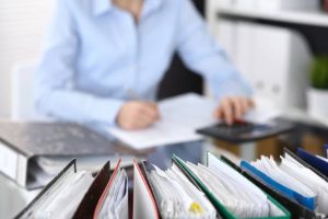 Binders with papers are waiting to be processed with businesswoman or secretary back in blur.