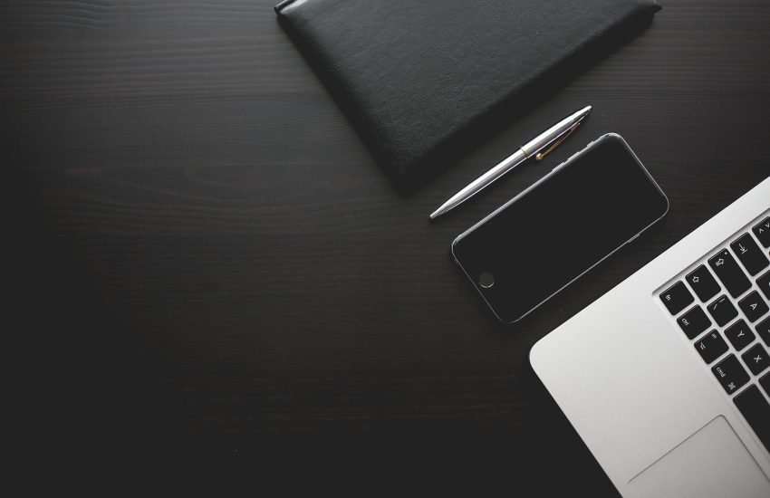 Black desk with phone and laptop.