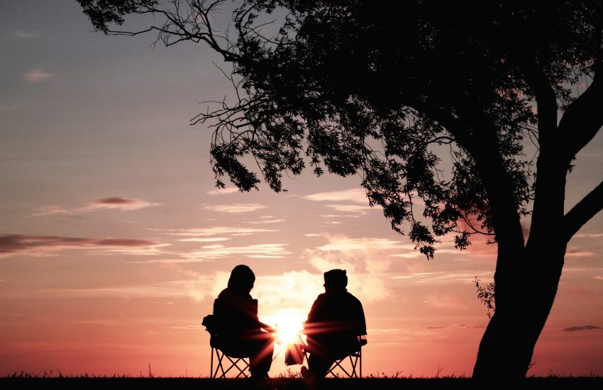 Silhouette of a tree and elderly couple with a sunset.